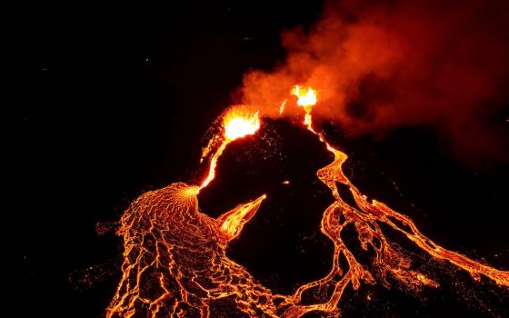 Orange lava flowing down dark volcano at night
