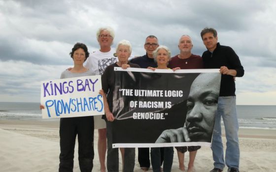 Seven people on a beach holding signs; one says "Kings Bay Plowshares," the other features a portrait of Martin Luther King, Jr. 