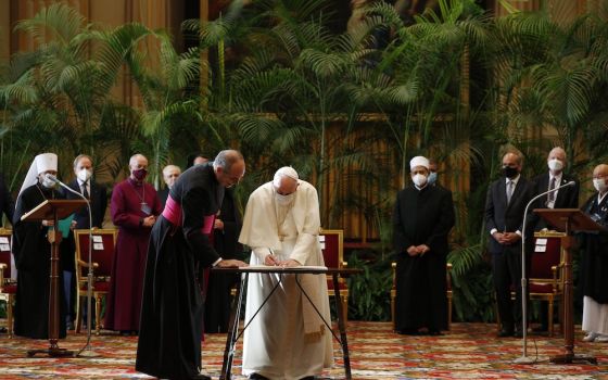 Flanked by leaders of major world religions Oct. 4 at the Vatican, Pope Francis signs a joint appeal to government leaders to curb global warming and heal the planet. (CNS/Paul Haring)