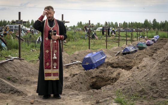 A priest prays Aug. 11 for unidentified civilians killed by Russian troops during Russian occupation in Bucha, on the outskirts of Kyiv, Ukraine. (AP/Efrem Lukatsky)