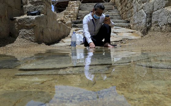 Syrian Christian Zuhair Al-Sahawi immerses his hand in water at the Bethany Beyond the Jordan baptismal site on the east bank of the Jordan River in Jordan June 8. (AP/Raad Adayleh)