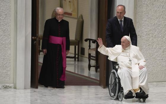 Pope Francis arrives in a wheel chair in the Paul VI hall to attend an audience with pilgrims from central Italy at the Vatican, Saturday, May 14, 2022. (AP Photo/Gregorio Borgia)