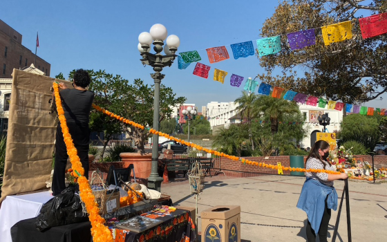 Teresa Velez, left, and her daughter-in-law Olivia Butler, hang marigold garlands on an "ofrenda" in Los Angeles Plaza for a COVID-constrained Día de los Muertos observance. Day of the Dead celebrations have been going on here for more than 30 years. (NCR