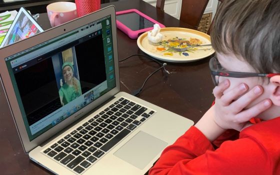 Jaxon, a second-grader at Holy Family Catholic Academy in Inverness, Illinois, watches a video from one of his teachers on a laptop at his dining room table. (Jamie Breeden)