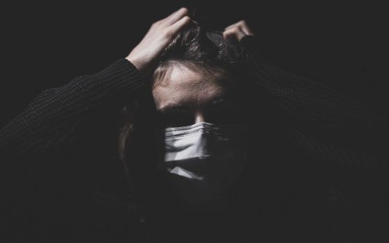 Darkened room image of woman in mask pulling at her hair in stress