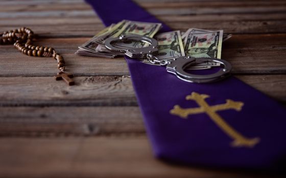 Image of a rosary, US currency, handcuffs and a cross on a wooden table (Dreamstime/Djedzura)
