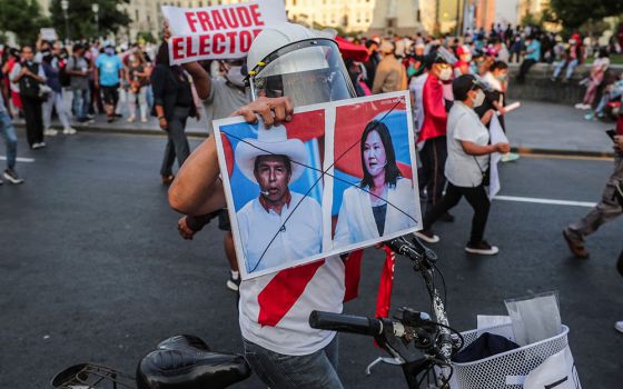 A protester in Lima, Peru, on April 17 holds a sign showing crossed out images of candidates Pedro Castillo and Keiko Fujimori, who will face each other in the second round of Peru's presidential election on June 6. (Newscom/Reuters/Sebastian Castaneda)