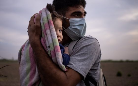 A migrant from Honduras cradles his daughter from the early morning cold and wind after crossing the Rio Grande into La Joya, Texas. Climate change is an underlying cause of migration from Central America and other regions of the world. (CNS photo/Adrees 