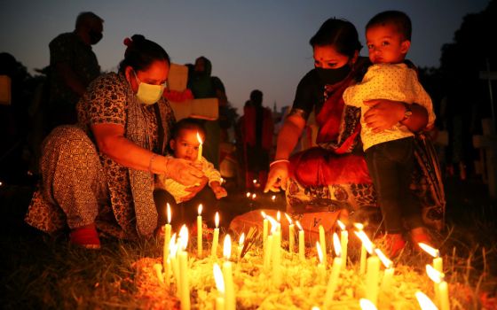 A woman helps a child to light a candle as they pray for the departed souls of their relatives at a cemetery in Dhaka, Bangladesh, during the feast of All Souls Nov. 2, 2021. (CNS/Reuters/Mohammad Ponir Hossain)