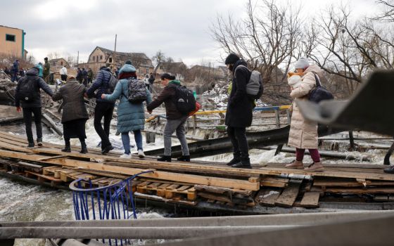 People fleeing advancing Russian forces file across wooden planks crossing the Irpin River below a destroyed bridge in Ukraine March 9. (CNS/Reuters/Thomas Peter)
