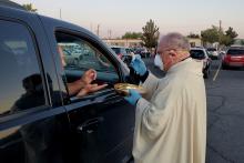 Bishop Peter Baldacchino wears a mask and gloves while giving Communion to a passenger of a vehicle during the Easter Vigil in the parking lot of the Cathedral of the Immaculate Heart of Mary in Las Cruces, New Mexico, April 11. (CNS)