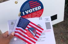 A sign, postcard and American flag with "I voted" stickers on them. (Unsplash/Janine Robinson)