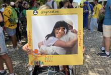 A young man puts his head through a cutout frame to take a photo "hugging" Pope Francis at the Synod of Bishops' booth in a park in Lisbon, Portugal, during World Youth Day Aug. 3. (CNS/Courtesy of the Synod Secretariat)