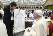 A brown-haired man looks down at the print that he is presenting to Pope Francis