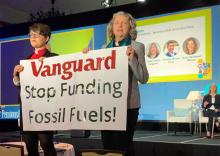 GreenFaith organizers Chelsea MacMillan, left, and Amy Brooks Paradise hold up a banner that reads, "Vanguard Stop Funding Fossil Fuels!" during an Oct. 23 investment industry conference at the Omni La Costa Resort in Carlsbad, California. (Courtesy of GreenFaith)