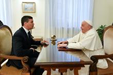 Pope sits at table, meeting with man.