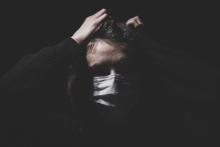 Darkened room image of woman in mask pulling at her hair in stress