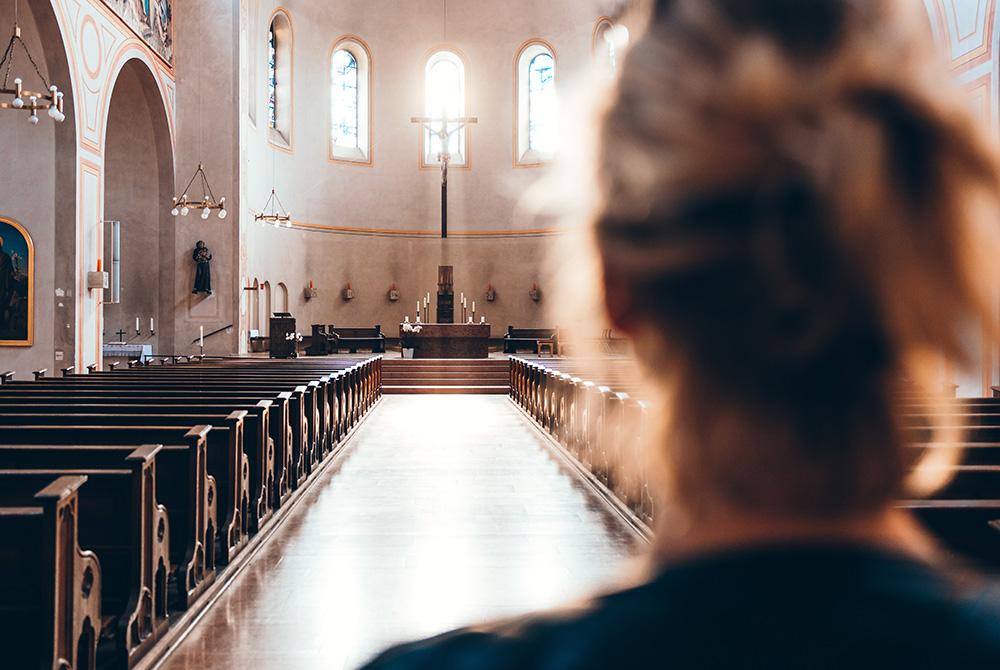 Photo illustration of a woman inside a church (Unsplash/Thomas Vitali)