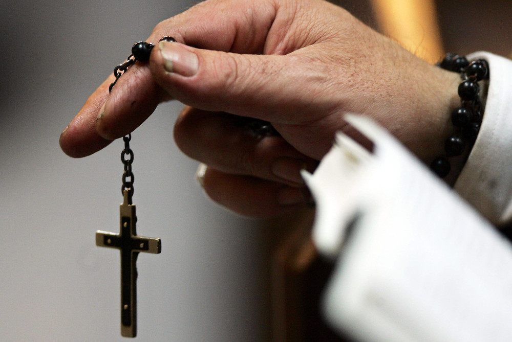 A worshiper is pictured in a file photo holding a rosary during Mass at St. Mary's Cathedral in Edinburgh, Scotland. (CNS/Reuters/David Moir)