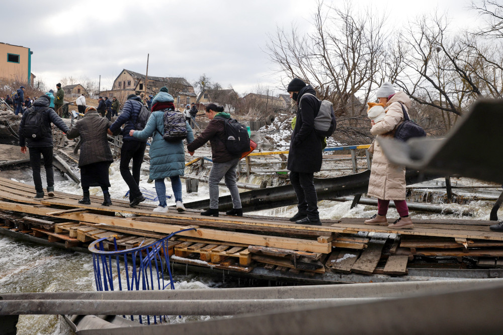 People fleeing advancing Russian forces file across wooden planks crossing the Irpin River below a destroyed bridge in Ukraine March 9. (CNS/Reuters/Thomas Peter)